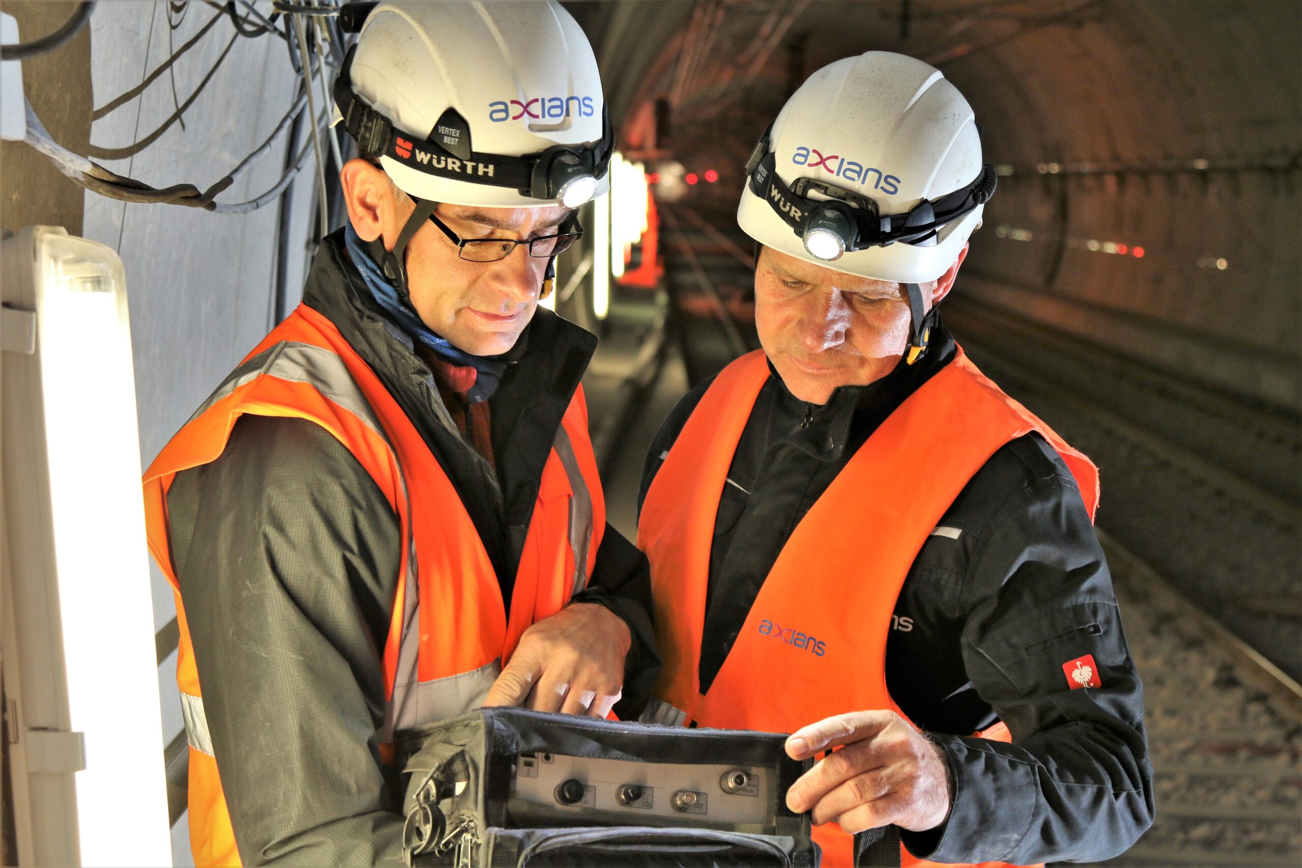 Zwei Männer in Axians Kleidung, mit Warnwesten und Hemd, setzen ein 5G-Campusnetz in einem Tunnel um.